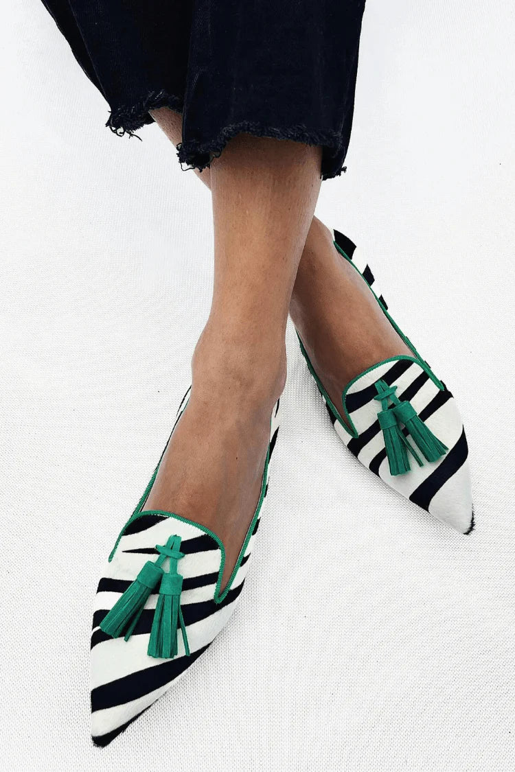 A woman wearing black-and-white zebra-stripe pointed flats finished with green tassels