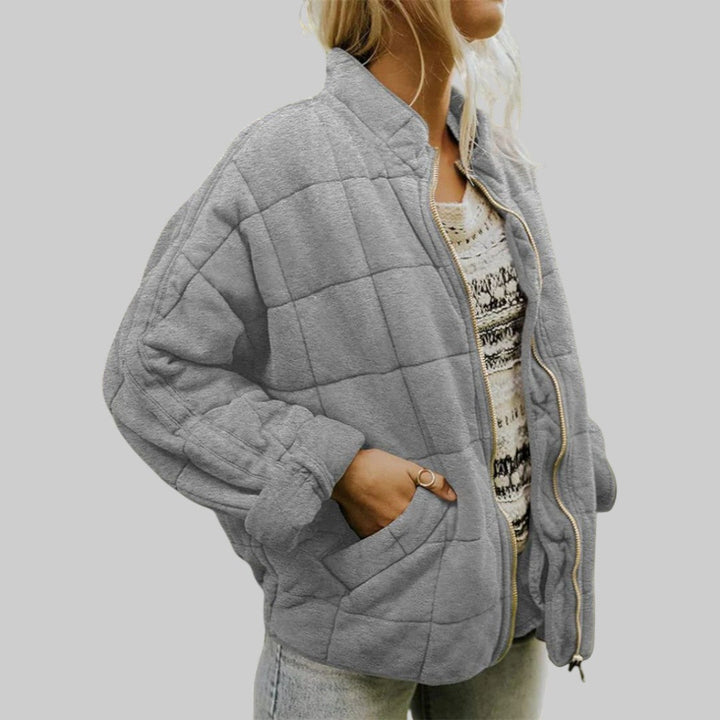 A woman wearing an oversized blush pink quilted jacket with a stand collar and zip front, hand in the pocket.