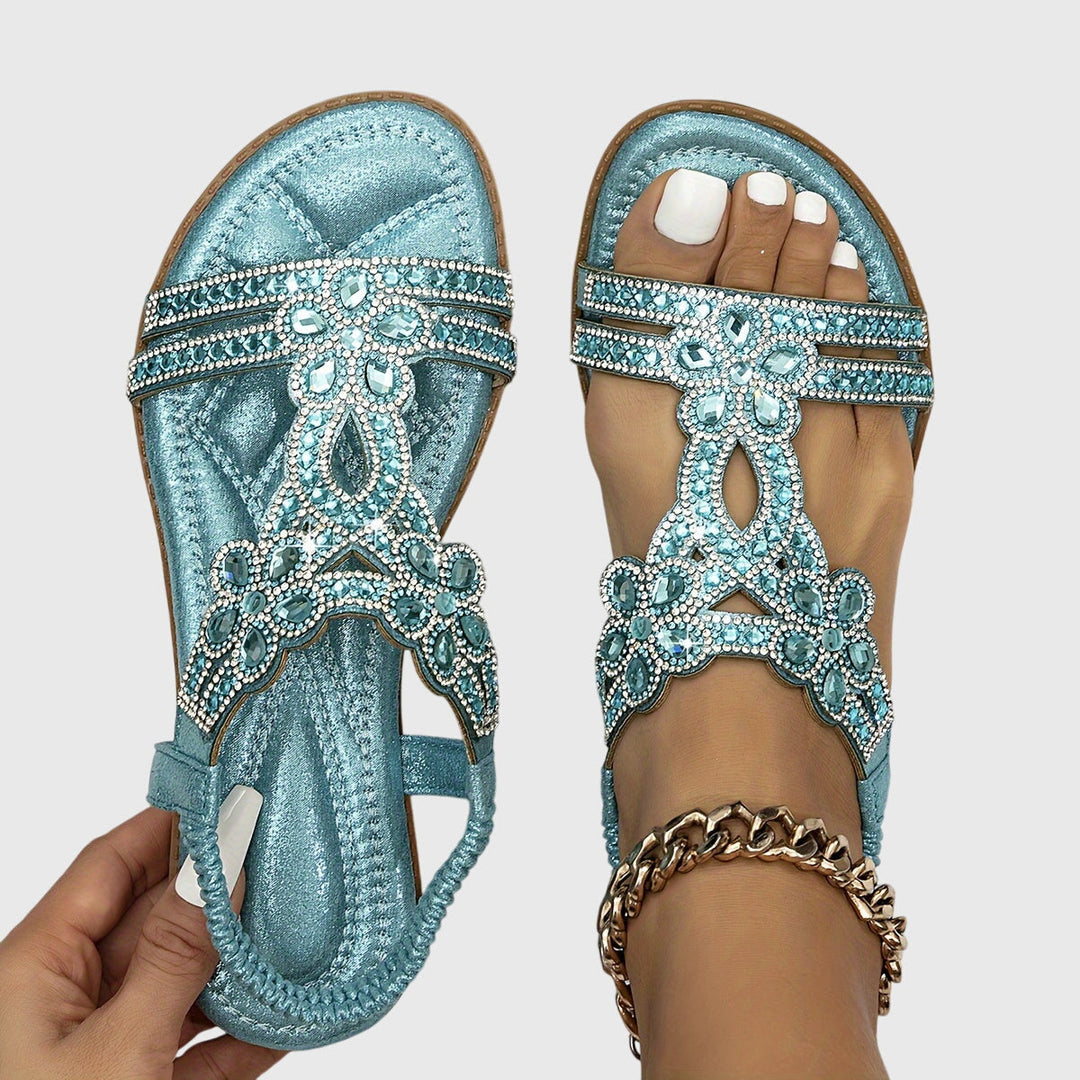 A woman wearing sky blue jewelled sandals with sparkling stones across the straps and a stretchy slingback.