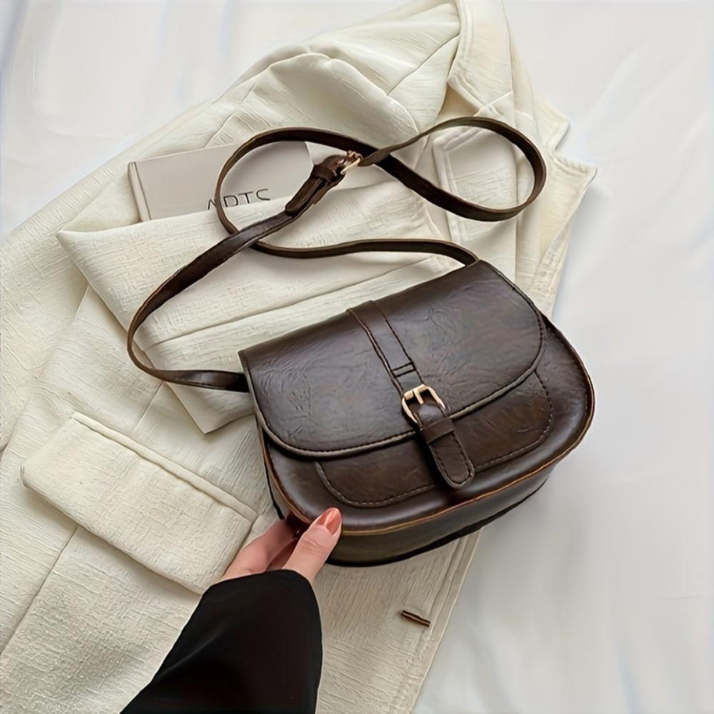 A woman carrying a crossbody satchel at her hip while out for a walk in town.