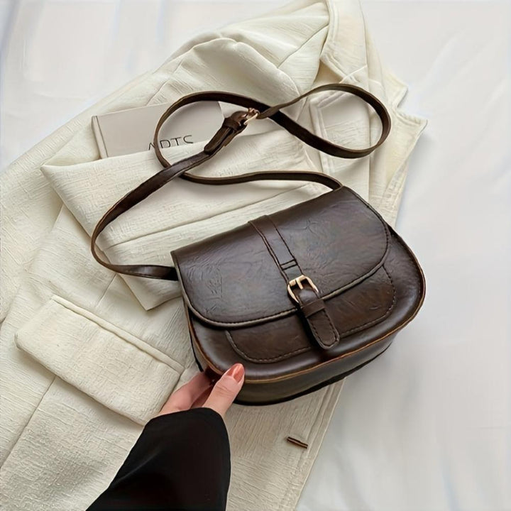 A woman carrying a crossbody satchel at her hip while out for a walk in town.