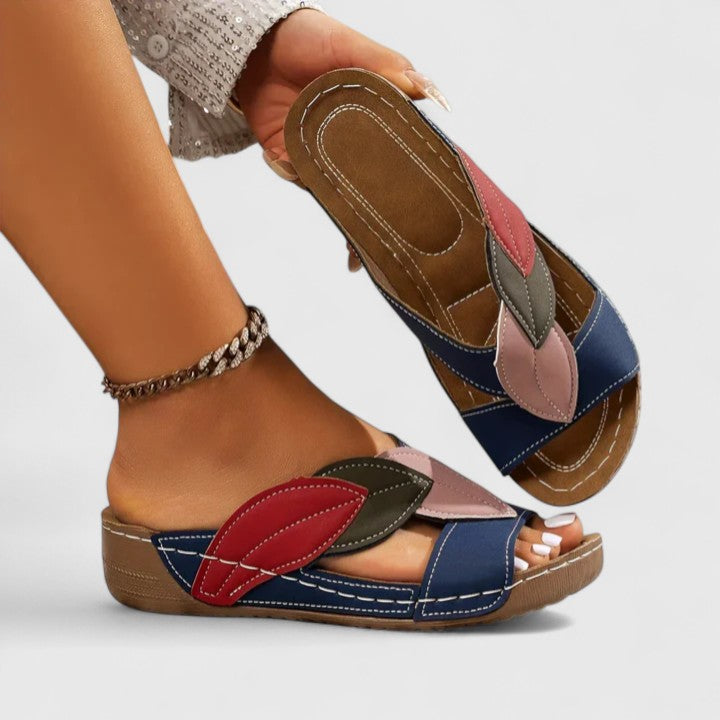 A woman wearing colourful leaf-print sandals with a cushioned insole and easy slip-on design.