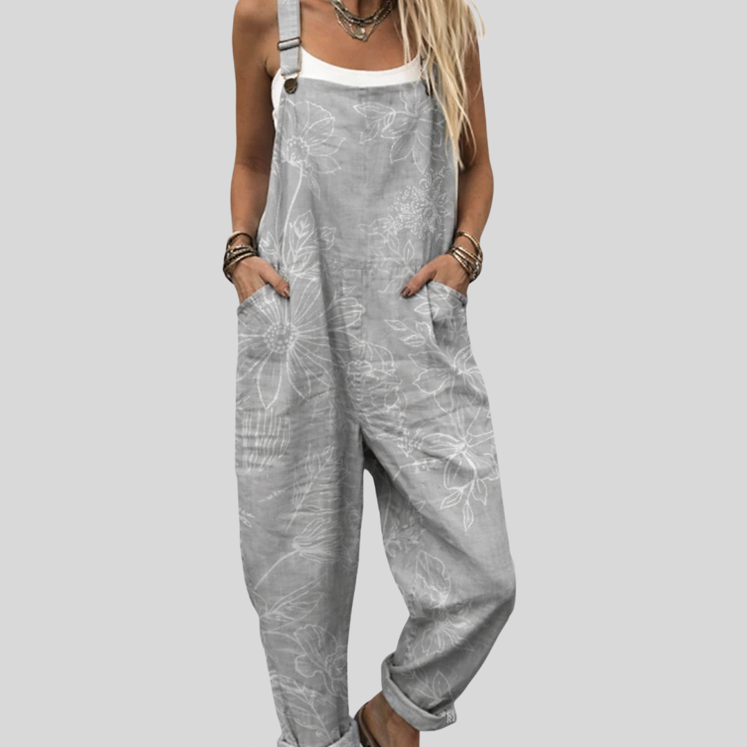A woman wearing relaxed light-grey overalls with a large white outline floral print and a white top.