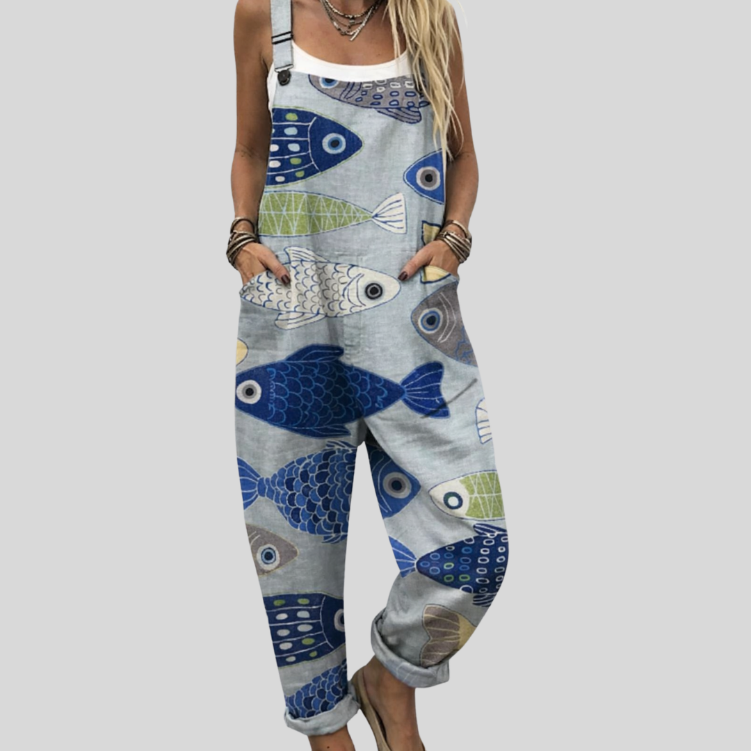 A woman wearing grey overalls printed with blue and green fish, relaxed and at ease outdoors.