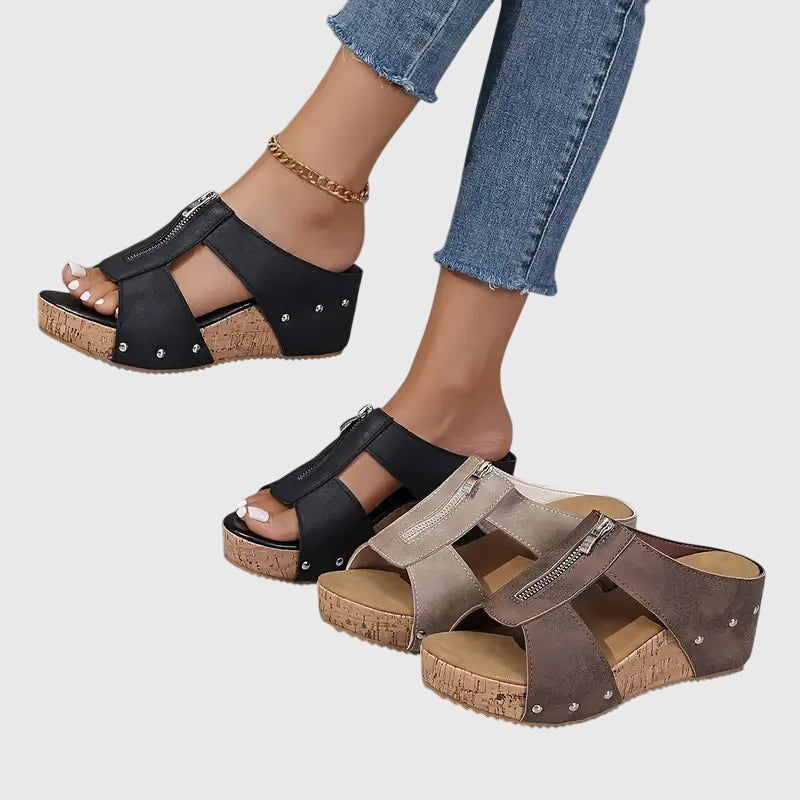 A woman wearing black zip-front wedge mules with a cushioned footbed and a broad platform sole.