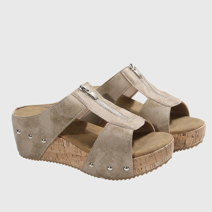A woman wearing black zip-front wedge mules with a cushioned footbed and a broad platform sole.