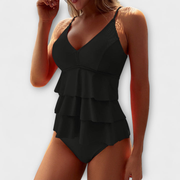 A woman by the pool in a solid-colour tiered ruffle swimsuit, poised and relaxed in the summer sun.
