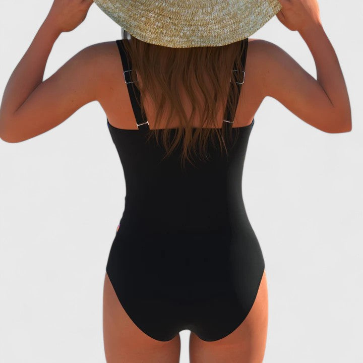 A woman by the water in an elegant printed swimsuit, poised and confident in the summer sun.