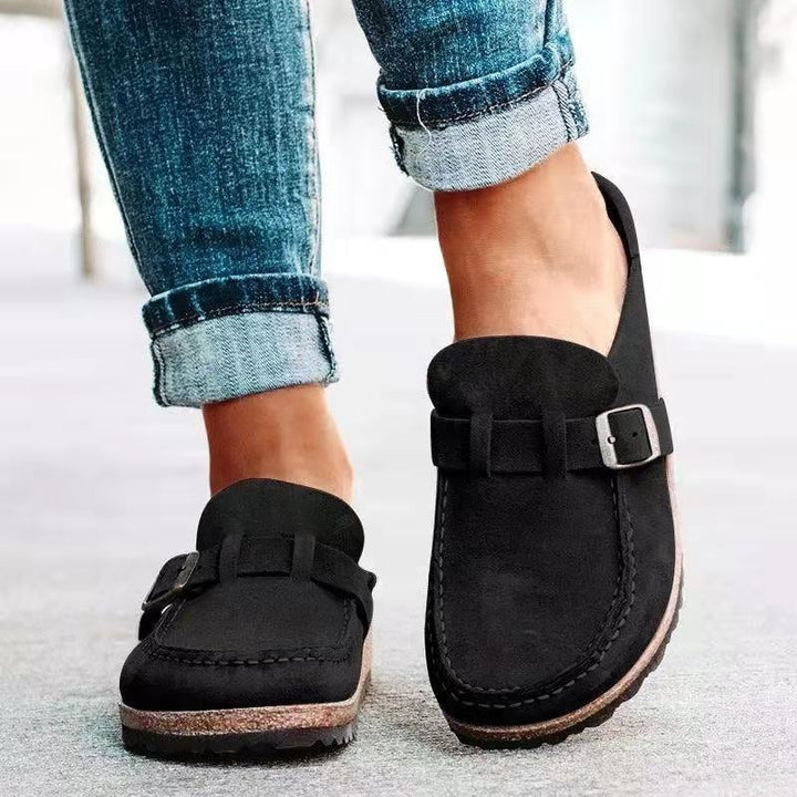 A woman wearing soft taupe buckle clog mules with cropped jeans on a city stroll.