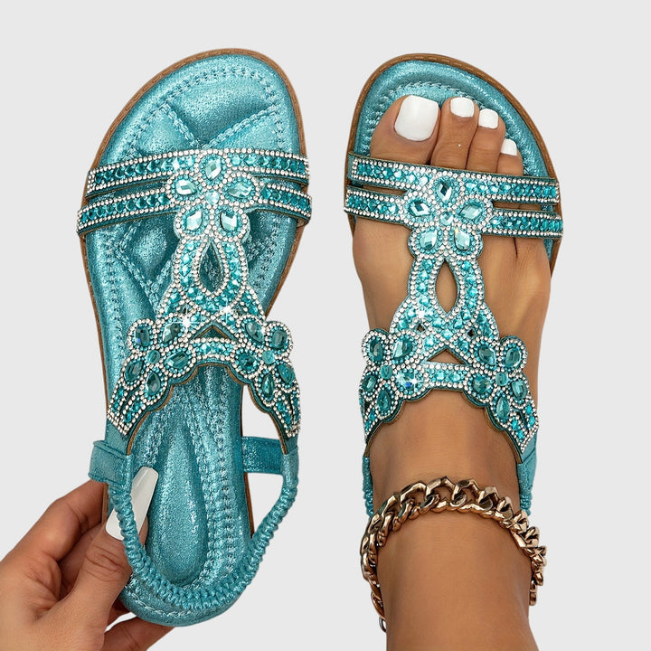 A woman wearing sky blue jewelled sandals with sparkling stones across the straps and a stretchy slingback.
