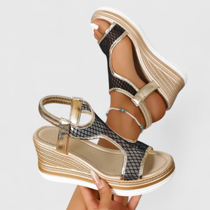 A woman wearing golden platform wedge sandals with a T-bar front, open-weave panels and a stretchy slingback.