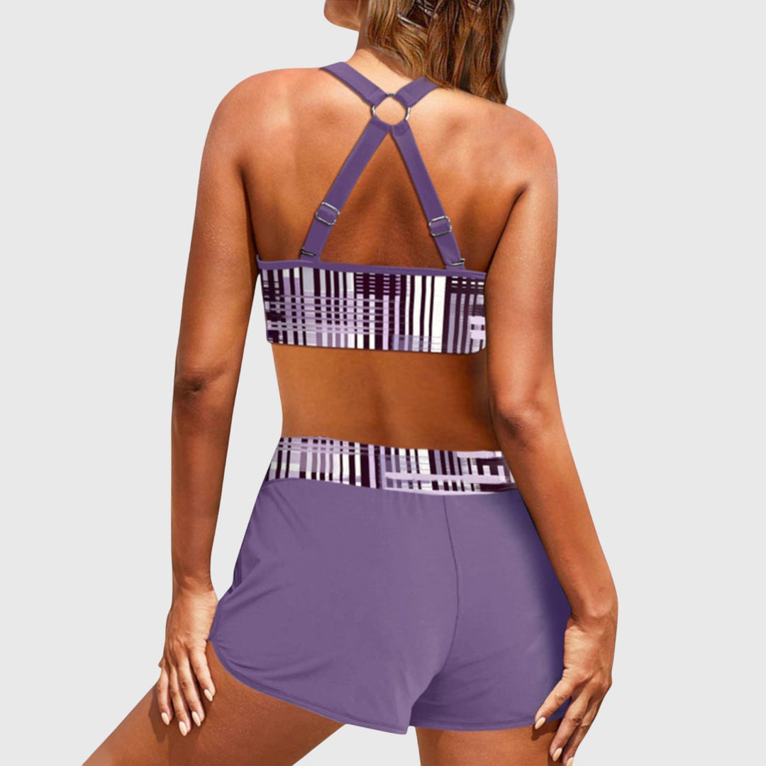 A woman at the beach in a striped bikini top with matching swim shorts, confident and relaxed in the sun.