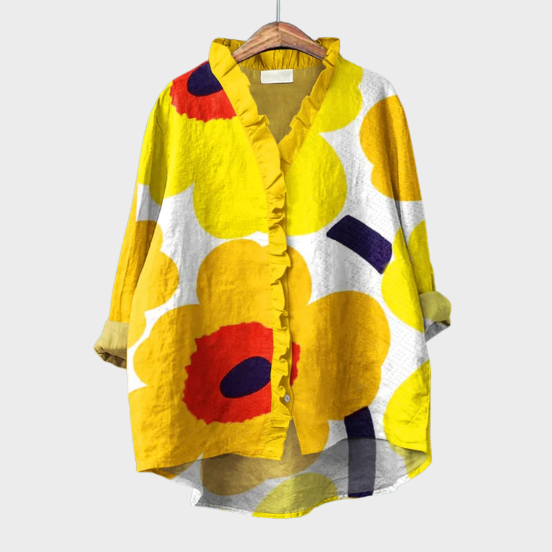 A woman wearing an elegant yellow patterned summer blouse, looking relaxed and polished on a warm day.
