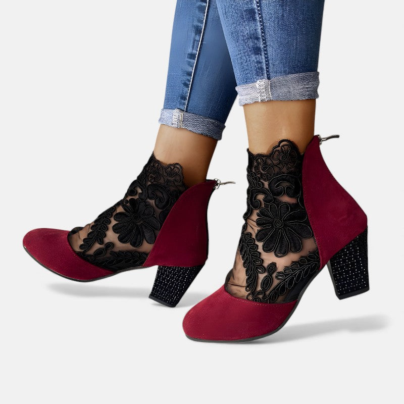 A woman wearing wine block-heel shoes with a sheer black floral-lace ankle overlay and a crystal-set heel