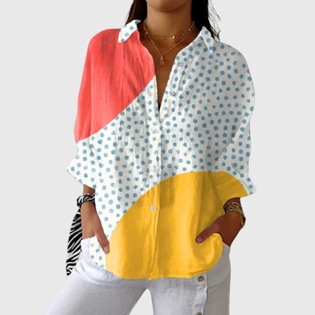 A woman wearing a loose colourful printed blouse with an elegant button front, styled with pants for a relaxed day out.
