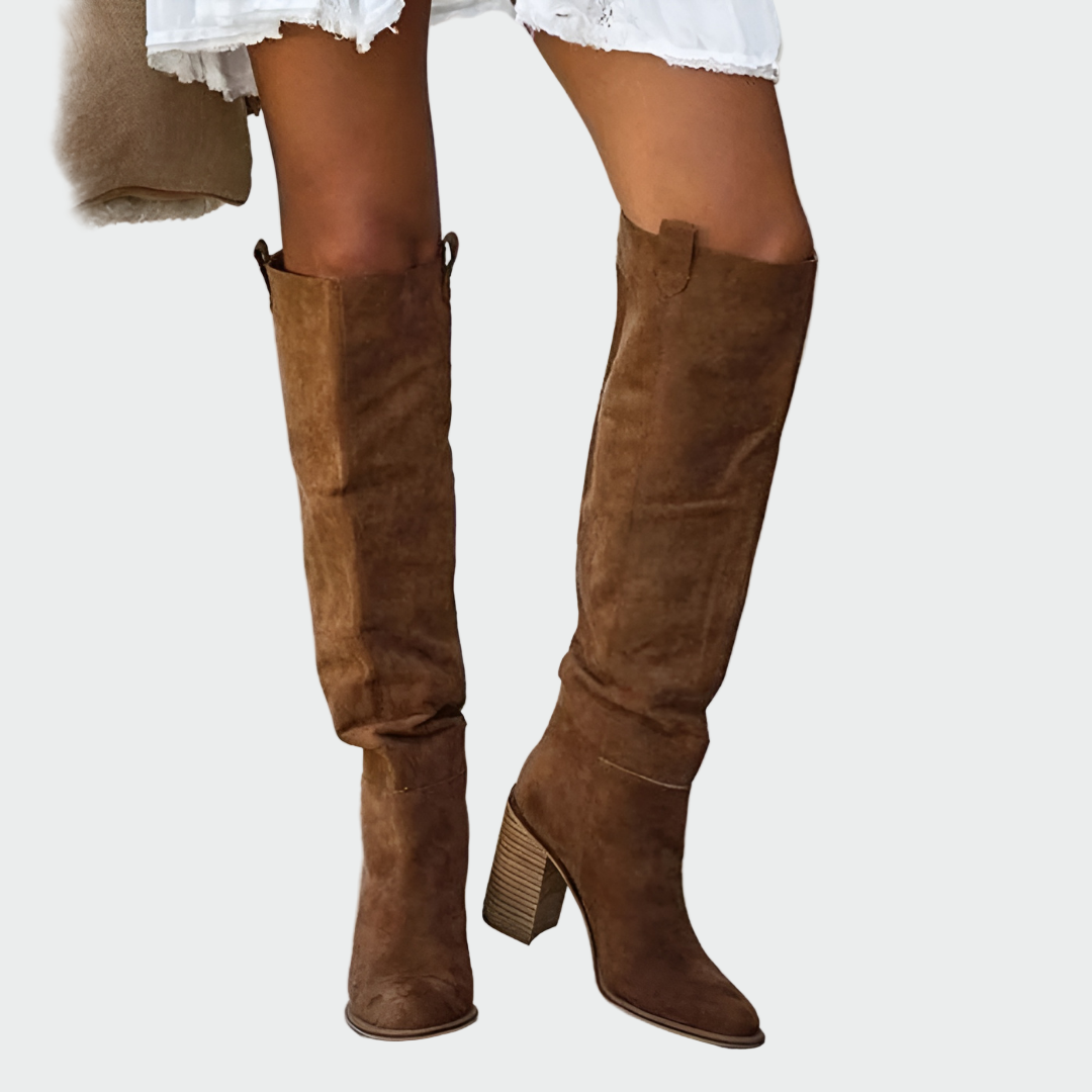 A woman in a dress wearing warm brown knee-high Western-style boots with a sturdy block heel.