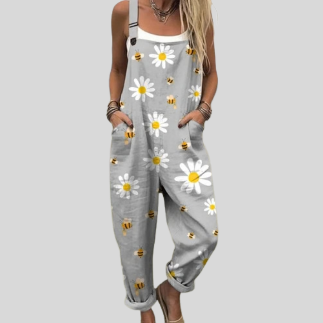 Woman wearing soft grey overalls printed with white daisies and little bees, standing relaxed and smiling.