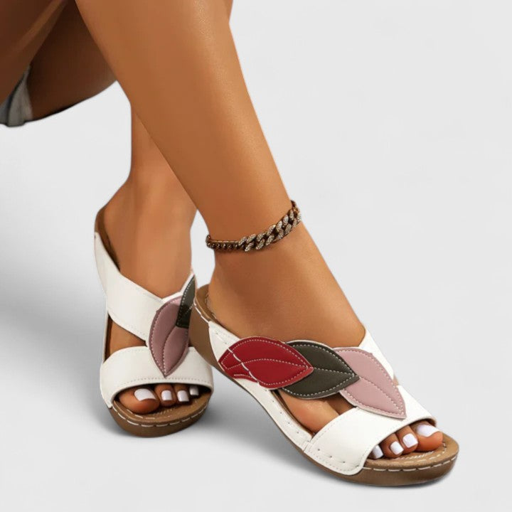 A woman wearing colourful leaf-print sandals with a cushioned insole and easy slip-on design.