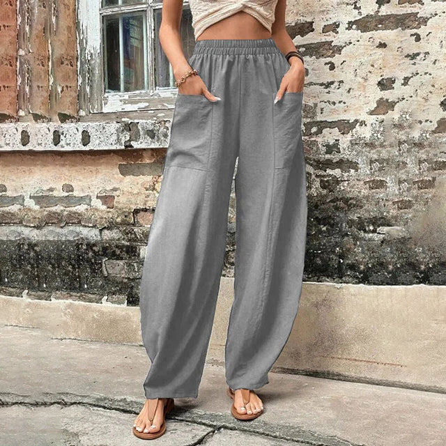 A woman walking in flowing wide-leg pants with big patch pockets and an elegant, draped silhouette.