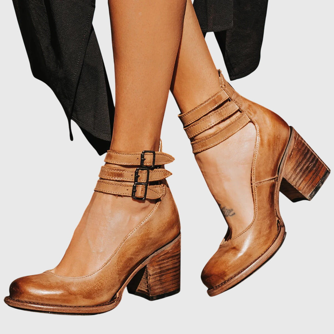 A woman wearing tan block-heel court shoes with buckled ankle straps, walking gracefully in a refined outfit.