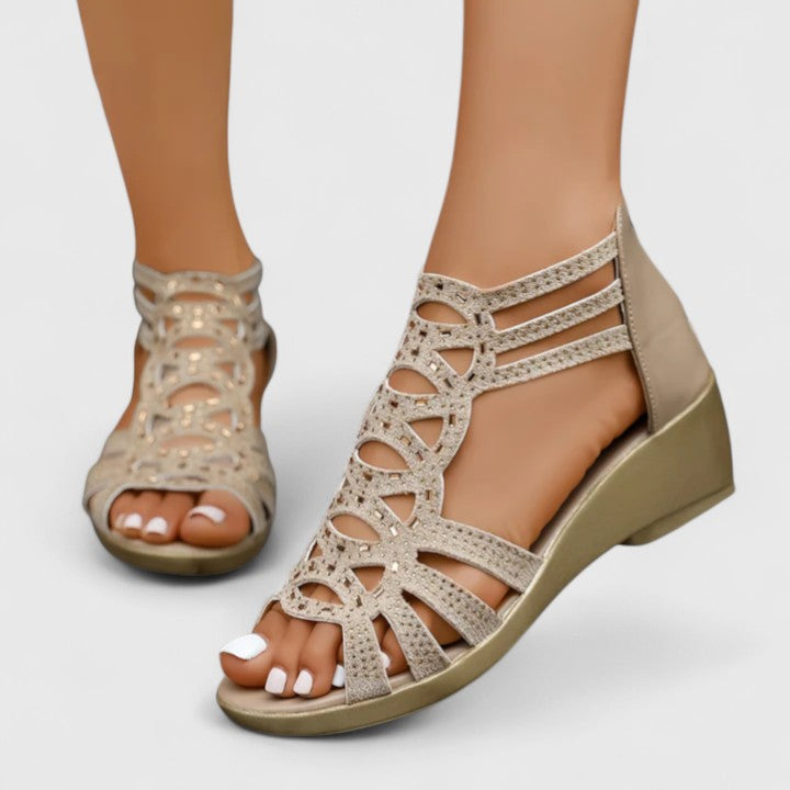 A woman wearing khaki sparkling cut-out wedge sandals with a low wedge heel and a back zip.