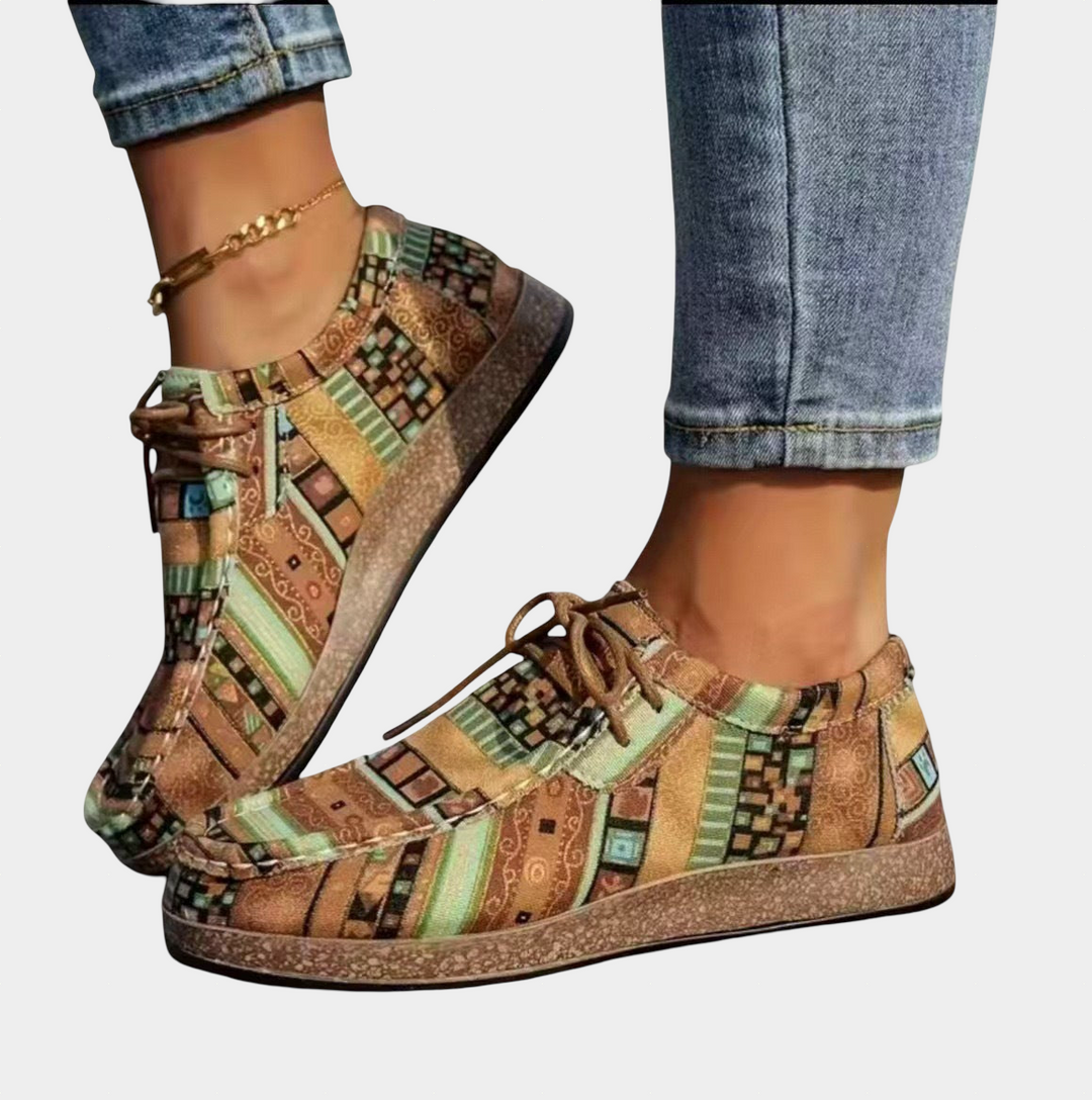 A woman standing in warm brown patchwork boho-print lace-up comfort shoes on a bright day.