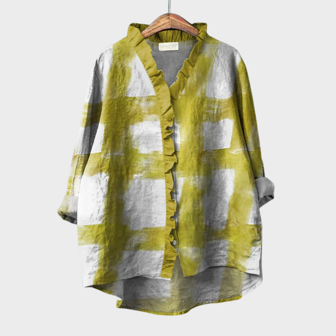 A woman wearing an elegant yellow patterned summer blouse, looking relaxed and polished on a sunny day.