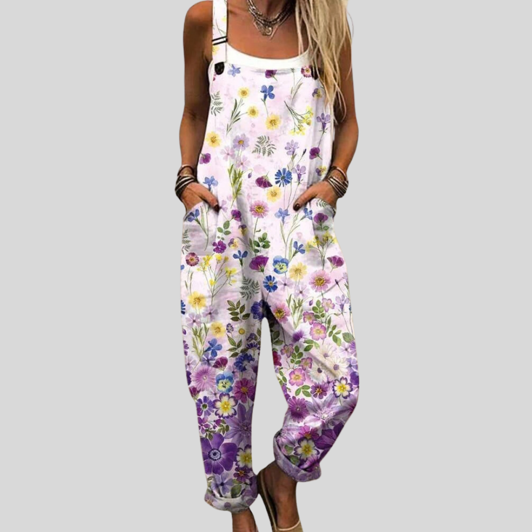 A woman wearing pale overalls printed with delicate lilac and violet wildflowers, relaxed outdoors.