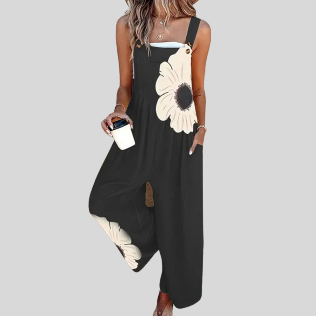 A woman wearing black overalls with one large cream-coloured flower and a simple top.