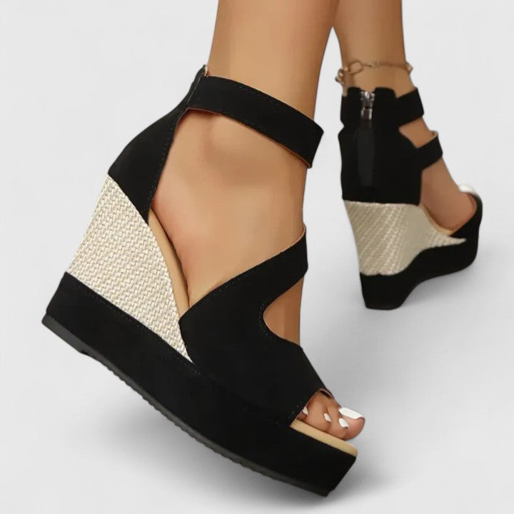 A woman in a summer dress wearing black crossover-strap heeled sandals, standing with easy confidence.