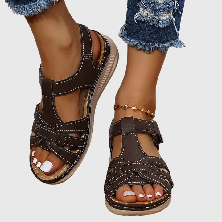 A woman wearing brown woven-effect strap sandals with a cushioned insole and adjustable strap.