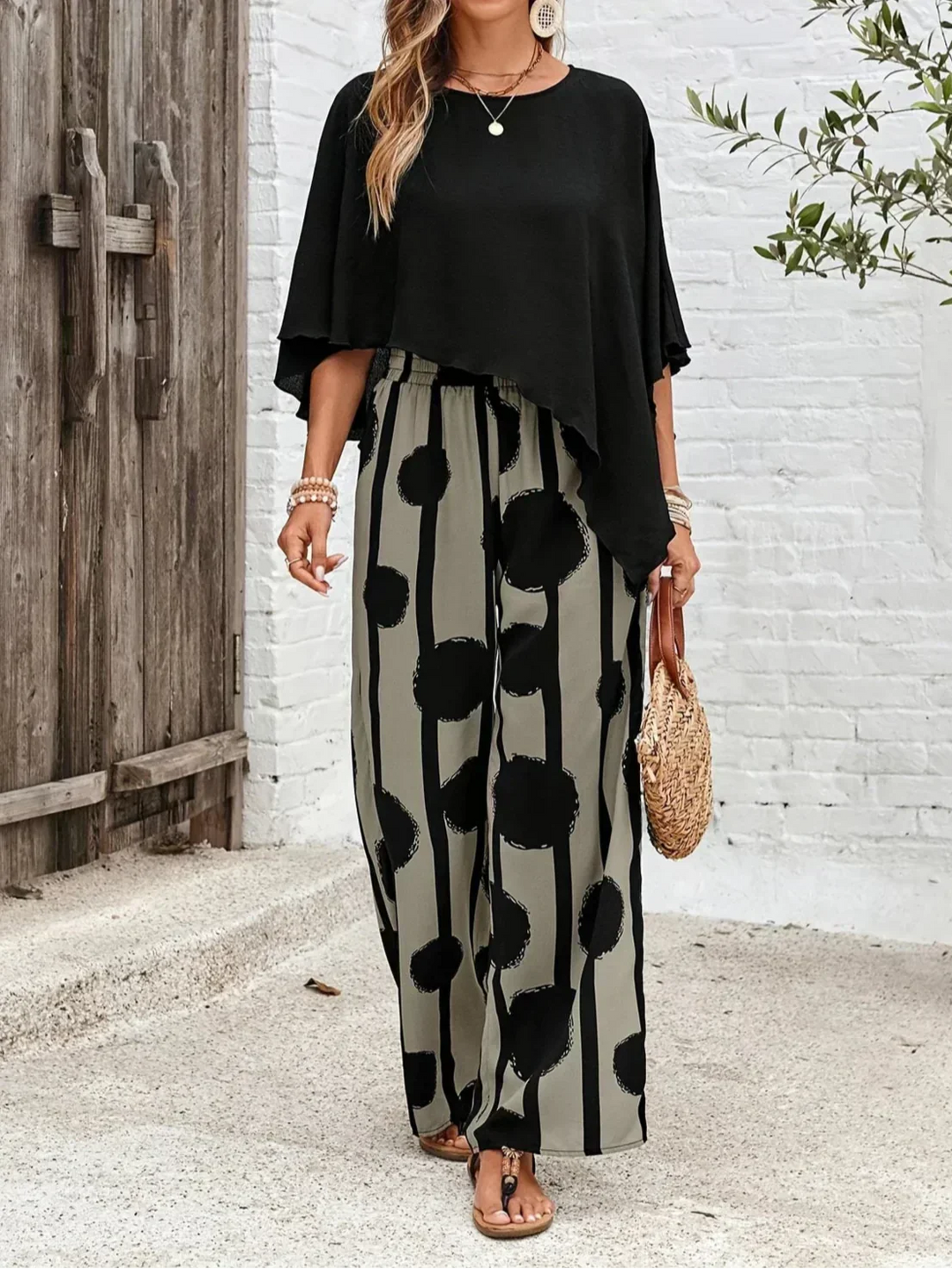 A woman wearing a draped asymmetric top with printed high-waisted wide-leg pants.