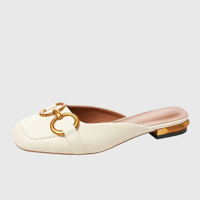 A cream closed-toe mule with a gold horsebit ring detail and a low heel.