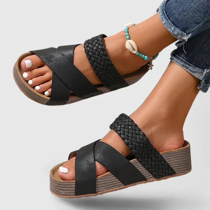 A woman strolling on a sunny street wearing beige woven comfort sandals with crossed straps.