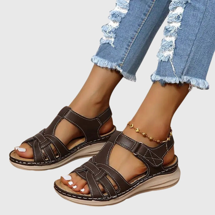 A woman wearing brown woven-effect strap sandals with a cushioned insole and adjustable strap.
