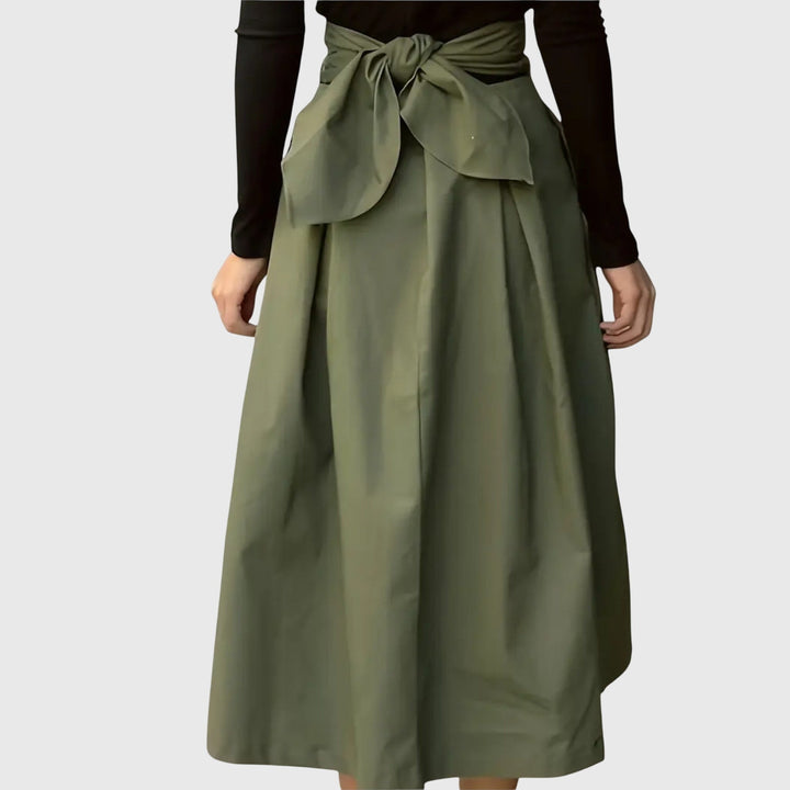 A woman wearing a flared green midi skirt with a belt detail at the waist.