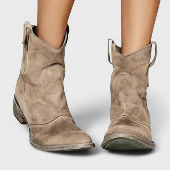 Woman wearing brown Western ankle boots with jeans, standing on a country lane.