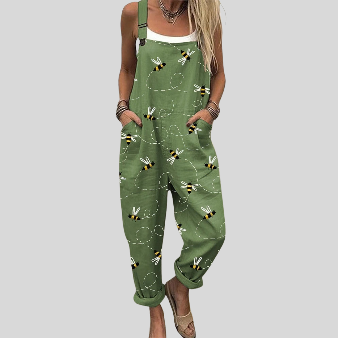 Woman wearing fresh green overalls printed with little bees among fine dots, standing relaxed and smiling.