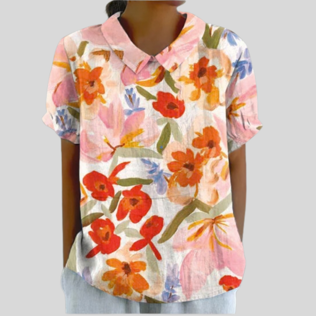 A woman wearing an elegant floral top with a neat polo collar, looking relaxed and put together.