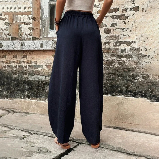 A woman walking in flowing wide-leg pants with big patch pockets and an elegant, draped silhouette.