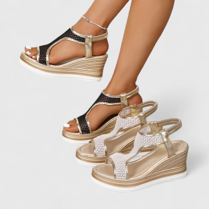 A woman wearing golden platform wedge sandals with a T-bar front, open-weave panels and a stretchy slingback.