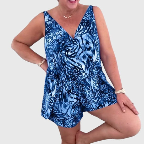 A woman in a blue printed swim playsuit with a flowing top and shorts, relaxed by the pool.