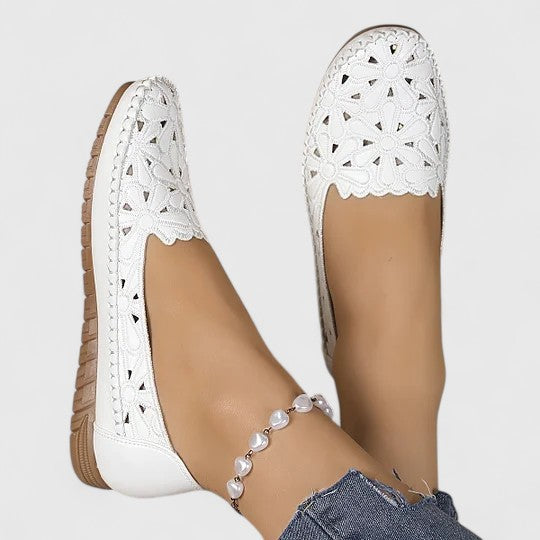 A woman wearing white floral cut-out slip-on flats on a warm, sunny day.