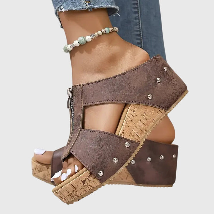 A woman wearing black zip-front wedge mules with a cushioned footbed and a broad platform sole.