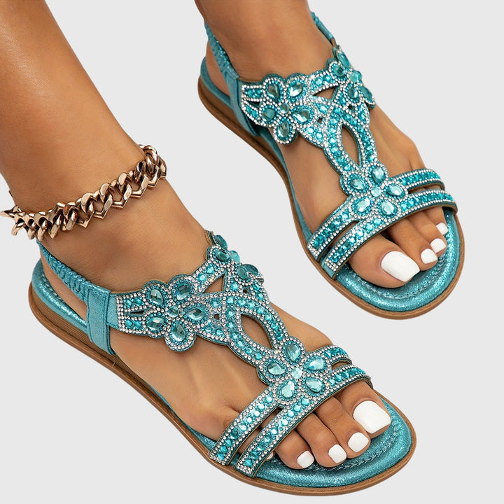 A woman wearing sky blue jewelled sandals with sparkling stones across the straps and a stretchy slingback.