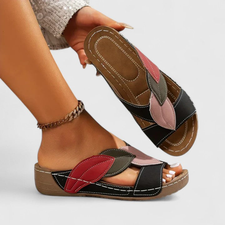 A woman wearing colourful leaf-print sandals with a cushioned insole and easy slip-on design.