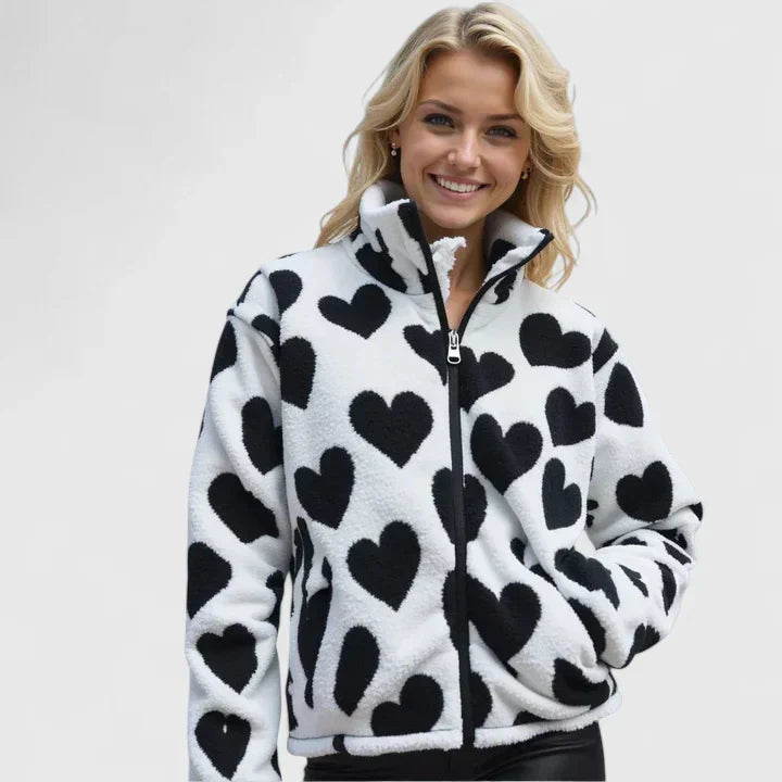 A woman wearing a plush white zip jacket with a bold black heart print and a high collar.