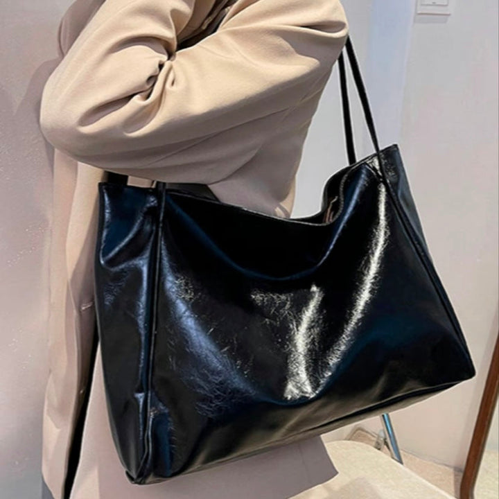 A woman wearing a glossy taupe shoulder bag over her shoulder at an evening occasion.