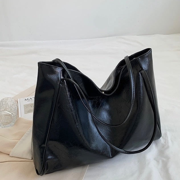 A woman wearing a glossy taupe shoulder bag over her shoulder at an evening occasion.
