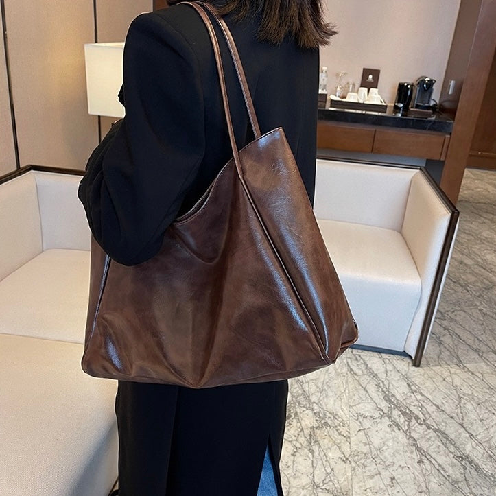 A woman wearing a glossy taupe shoulder bag over her shoulder at an evening occasion.